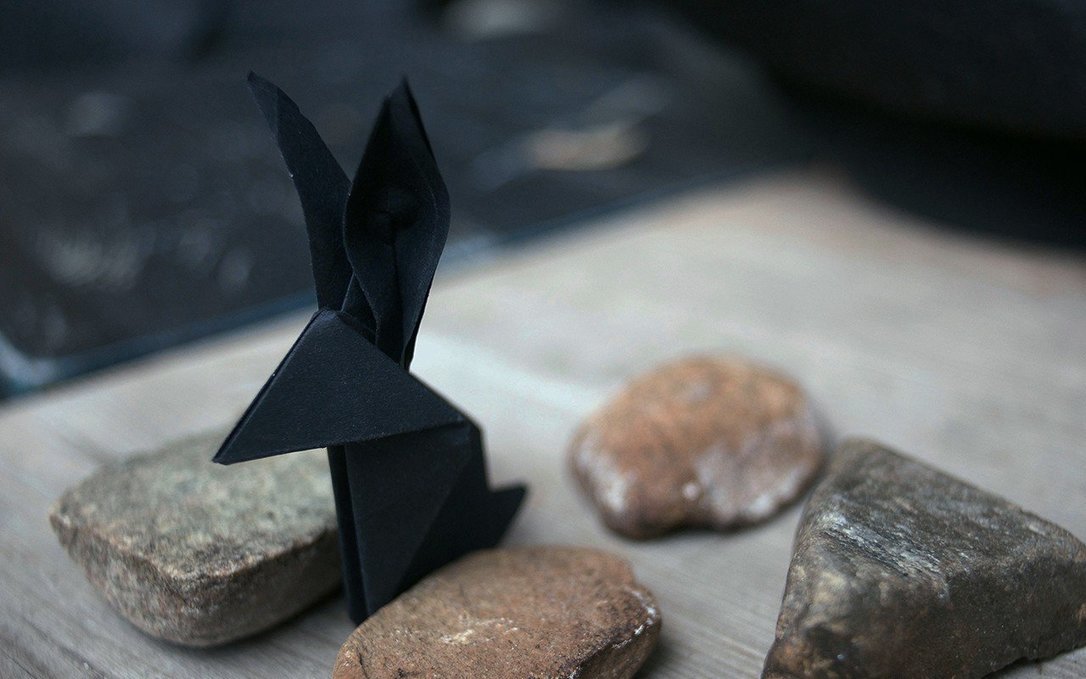 A black origami rabbit standing among rough stones.