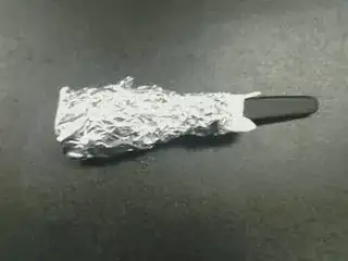 a knife, with the blade wrapped in a paper towel, which has aluminum foil wrapped around that