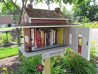 A "Little Free Library": a small box in the shape of a house that holds about twenty books. The box is placed in a residential neighborhood.