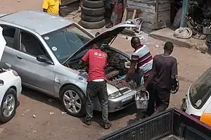 A car in the workshop with two mechanics working under the hood.