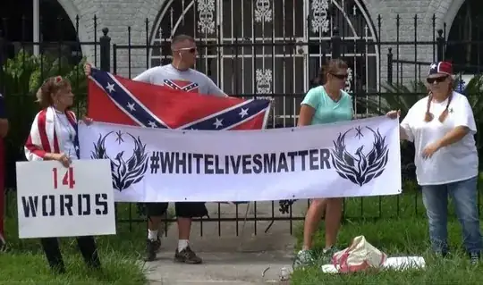 white supremacists holding up a "#whitelivesmatter" banner, a "14 words" poster, and a confederate flag