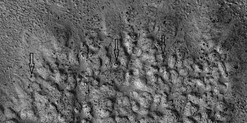 Closer view of ejecta, as seen by HiRISE under HiWish program.  Note:  Arrows show examples of boulders sitting in pits.