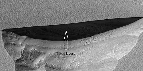 Close view of wall of triangular depression, as seen by HiRISE  layers are visible in the wall.  These layers contain ice.  The lower layers are tilted, while layers near the surface are more or less horizontal.  Such an arrangement of layers is called an  "angular unconformity".