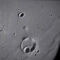 Lunar crater Krieger and vicinity, showing wrinkle ridges in the surrounding mare and sinuous rilles along the left edge, from Apollo 15