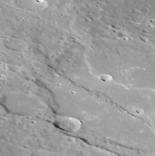 Oblique view of southern Thākur crater.  Two prominent lobate scarps deform the crater. These scarps form when one block of crust thrusts up and over another, and are thought to have formed due to a reduction in Mercury's surface area as its interior cooled and contracted. The face of a scarp indicates the direction these blocks have moved so, as we see it here, Tharkur has been squeezed from the top-right and from the bottom-left.
