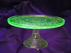A glass place on a glass stand. The plate is glowing green while the stand is colorless.