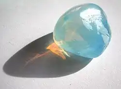 Tyndall effect in an opalite:it scatters blue light making it appear blue from the side, but orange light shines through.Opal is a gel in which water is dispersed in silica crystals.