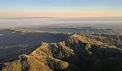 Loma Prieta (the peak just right of center) and other nearby peaks are decorated with television broadcast towers and other communication towers, serving the Santa Clara Valley. Fog-shrouded Monterey Bay and the Monterey peninsula are visible in the background in this late-afternoon approach to San José International Airport.