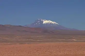 A snow covered flat-conical mountain rises above a ridge