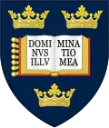 A shield displaying a coat of arms; on a dark blue background, an open book displays the words "Dominus illuminatio mea", with two gold crowns above and one below