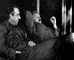 Two men sitting, looking relaxed. A dark-haired Bohr is talking while Einstein looks skeptical.