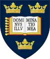 A shield displaying a coat of arms; on a dark blue background, an open book displays the words "Dominus illuminatio mea", with two gold crowns above and one below