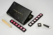 A black leather case with its contents: a candle and colour cards