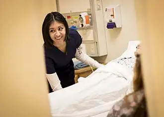 Smiling woman in scrubs leans over a hospital bed