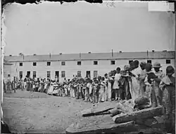 A contraband school, held outdoors. Note teacher, in coat and tie, on mound at left.