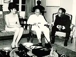 An elderly, smiling Du Bois sits in a chair, flanked by a man and woman also seated and smiling