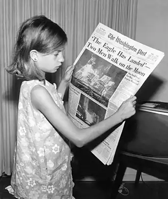 A girl reads a newspaper reporting that man has landed on the Moon (1969).