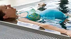 A pregnant woman floats in the corner of a swimming pool