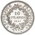 Piesă cu valoarea nominală de 5 franci, emisă în 1967, revers: circular, RÉPUBLIQUE FRANÇAISE, două ramuri înfrunzite (la stânga de laur, iar la dreapta de stejar), întretăiate la cele două capete; în centru, valoarea nominală și milesimul, pe trei rânduri: 10 / FRANCS / 1967