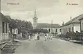 Biserica Romano-Catolică ,,Sfântul Anton de Padova'' Ilia, Curtea Bisericii Romano-Catolice Ilia, Piața ,,Sfântul Anton de Padova'' Ilia cu câțiva locuitori ai satului Ilia: femei și bărbați îmbrăcați în straie țărănești de sărbătoare discutând în centru iar pe margine o serie de case vechi cu terenuri anexate din Ilia și Pretura Maghiară Ilia din centrul istoric(vechi) al  satului Ilia. După claritatea fotografiei putem afirma că ea a fost realizată cu un aparat de fotografiat ,,Holzcamera  fabricat în Germania la sfarsitul secolului al XIX-lea - fotografie realizată în anul 1910