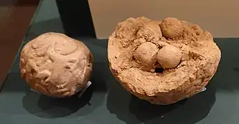 Două bulla (sau „plicuri” de lut); una sigilată, cealaltă spartă cu jetoane vizibile.