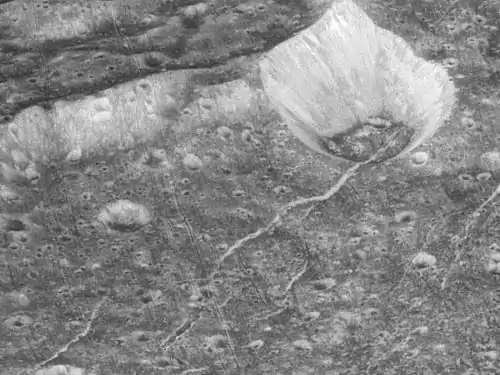 Crop of preceding image. The bowl-shaped crater at upper right has bright streaks on its walls, and dark material on its floor. To its lower left can be seen an arcuate fracture postdated (covered) by a small crater's ejecta, which in turn is postdated (incised) by parallel fractures.