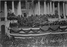 Photograph of a crowd in front of Capitol building decorated with patriotic bunting