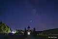 Mănăstirea Sihăstria Voronei, vedere nocturnă. Turla de la intrarea în mănăstire, încadrată între planetele Jupiter și Saturn, în dreapta Calea Lactee.