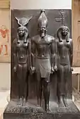 Statuie a lui Menkaura (în centru), alături de Hathor (în stânga) și Cynopolis; 2551–2523 î.Hr.; șist; înălțime: 95.5 cm; Muzeul Egiptean (Cairo)