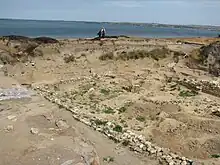 Rămășițele unui perete al unei mici structuri sunt văzute în prim plan, pe fundal este vizibilă Marea Azov.