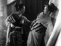 Une femme en kimono (Kinuyo Tanaka) aggripe d'une main le kimono d'une femme (Toshiko Iizuka) qui se cambre en arrière et de l'autre la menace d'un couteau (image en noir et blanc).