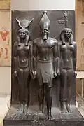 Statuie a lui Menkaura (în centru), alături de Hathor (în stânga) și Cynopolis; 2551–2523 î.Hr.; șist; înălțime: 95.5 cm; Muzeul Egiptean (Cairo)