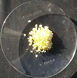 Watch glass on a black surface with a small portion of yellow crystals