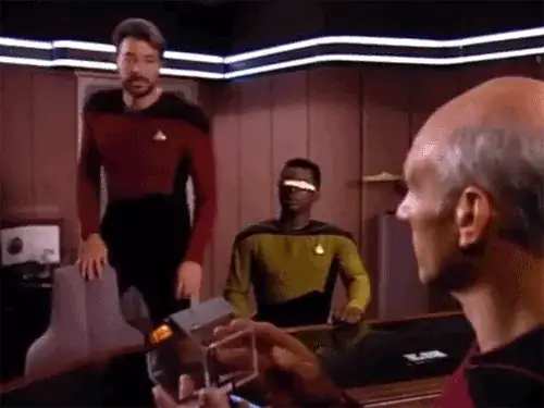 Commander Riker steps over a chair to sit on it