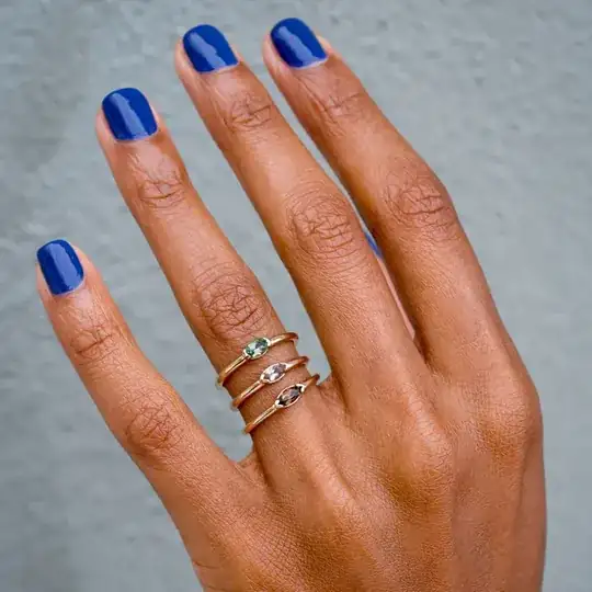A hand wearing three thin rings on the 4th finger